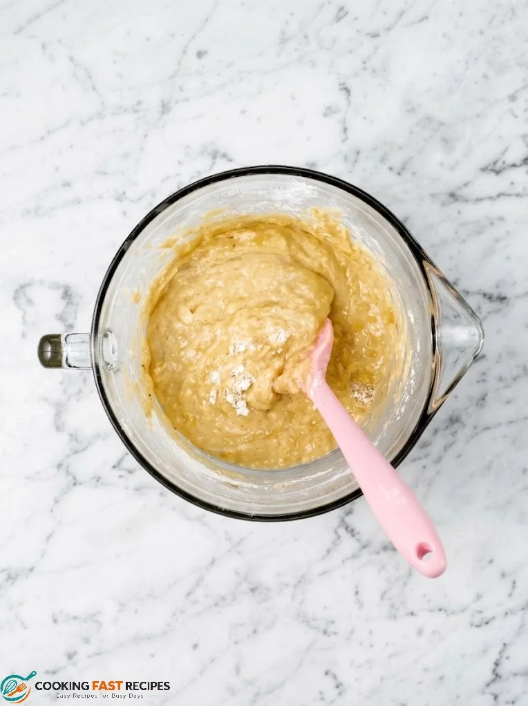Banana bread batter gently mixed in one bowl with a wooden spatula