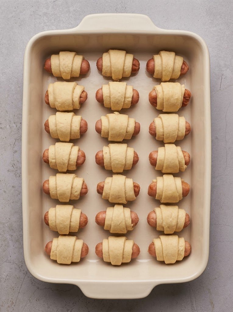 Unbaked pigs in a blanket arranged on a parchment-lined baking sheet